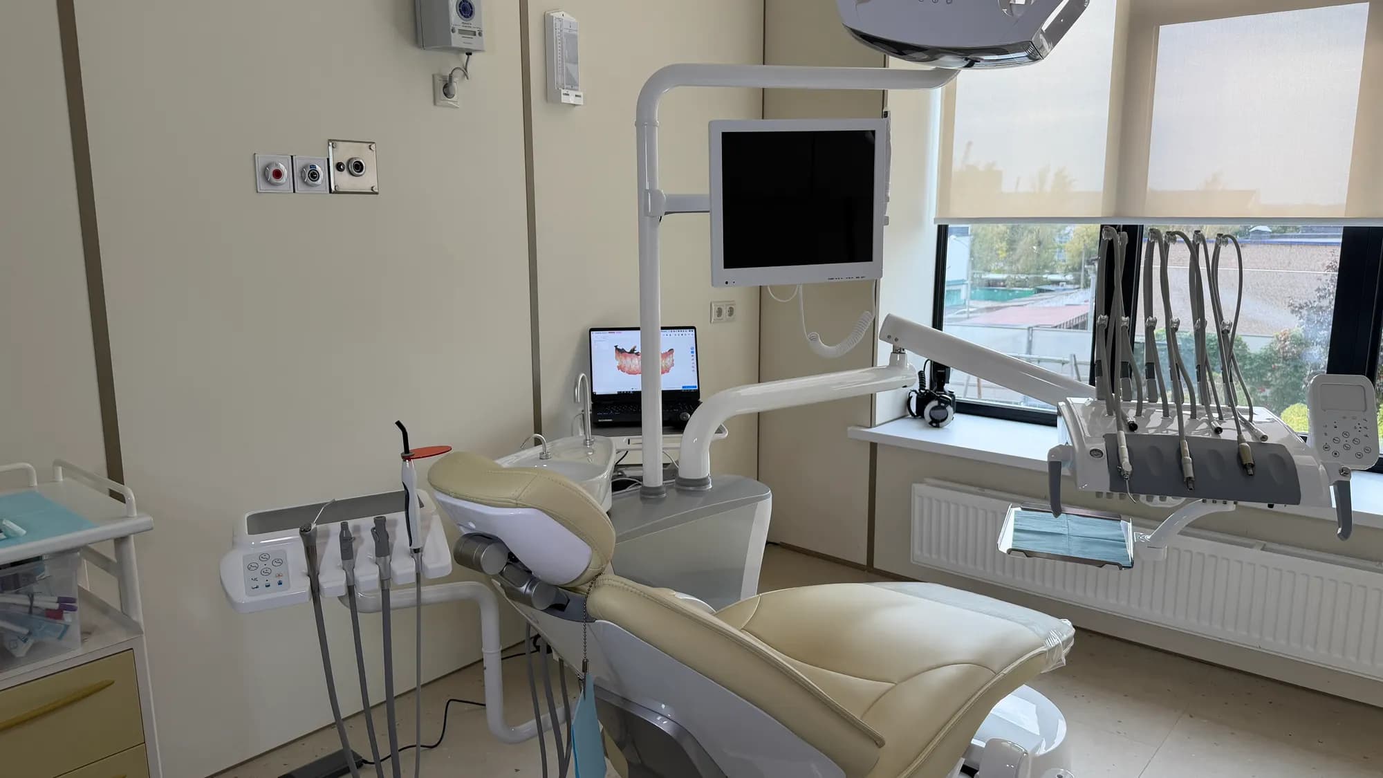Treatment room of the dentistry and maxillofacial surgery center: a dental chair by the window, a monitor and a 3D model of teeth on a laptop screen