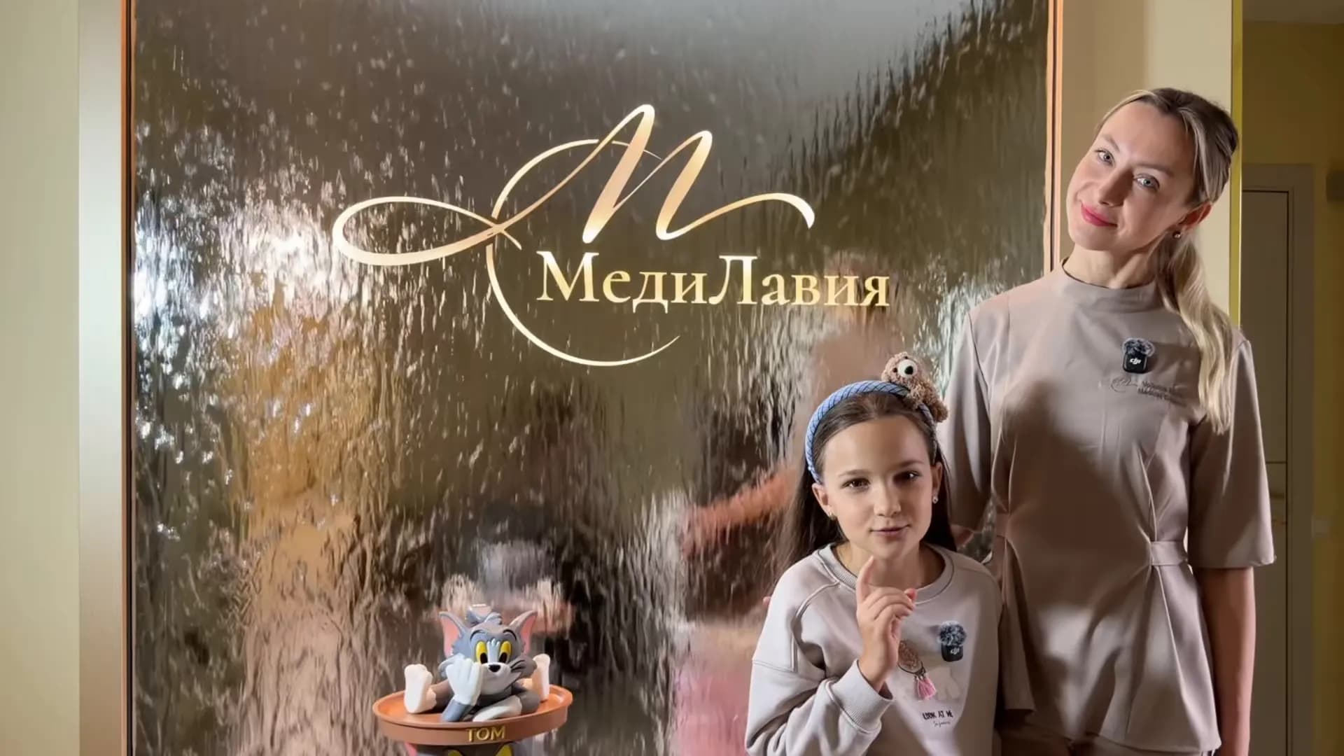 A children’s center team member and a girl in front of the water wall with the MediLavia logo