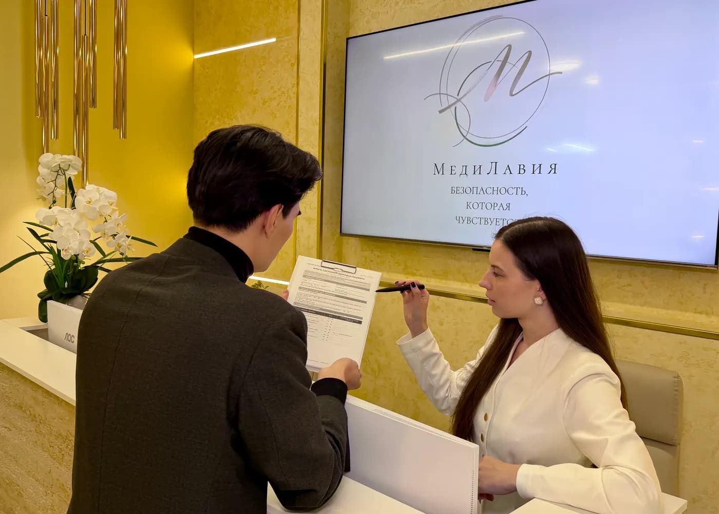 An administrator helps a patient fill in a form at the reception desk